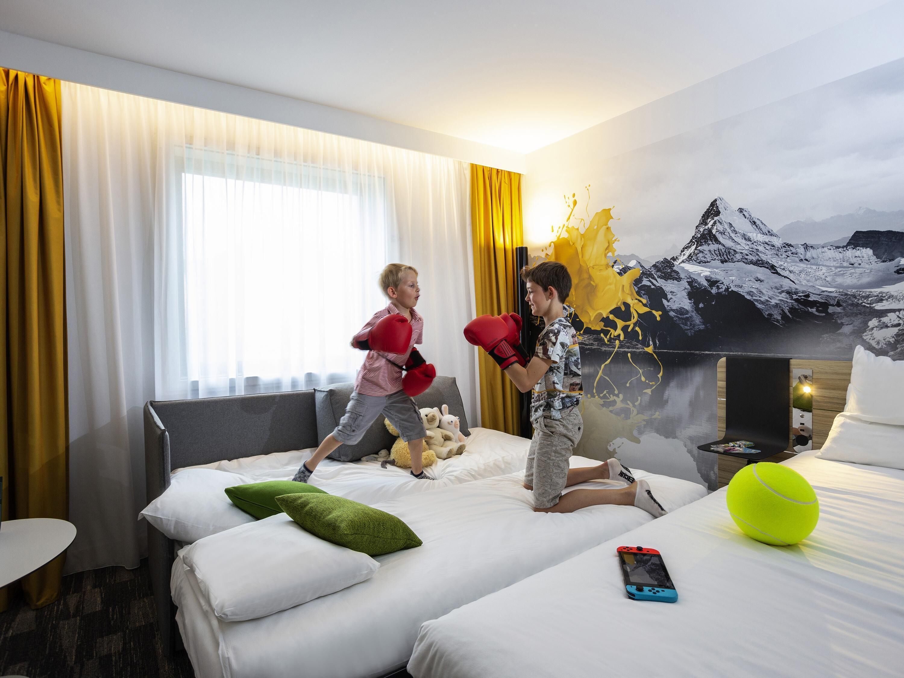 A hotel room with a bed, pillows, a TV, and a painting of a mountain landscape.