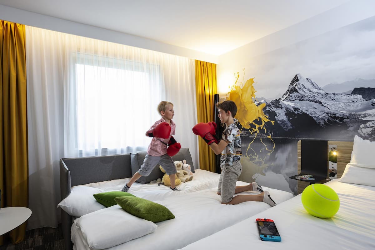 A hotel room with a bed, pillows, a TV, and a painting of a mountain landscape.