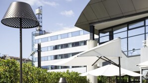 An outdoor dining area with a table set for breakfast, including fruits, juice, and pastries, with a modern building in the background. - Novotel Annecy Centre (Annecy)