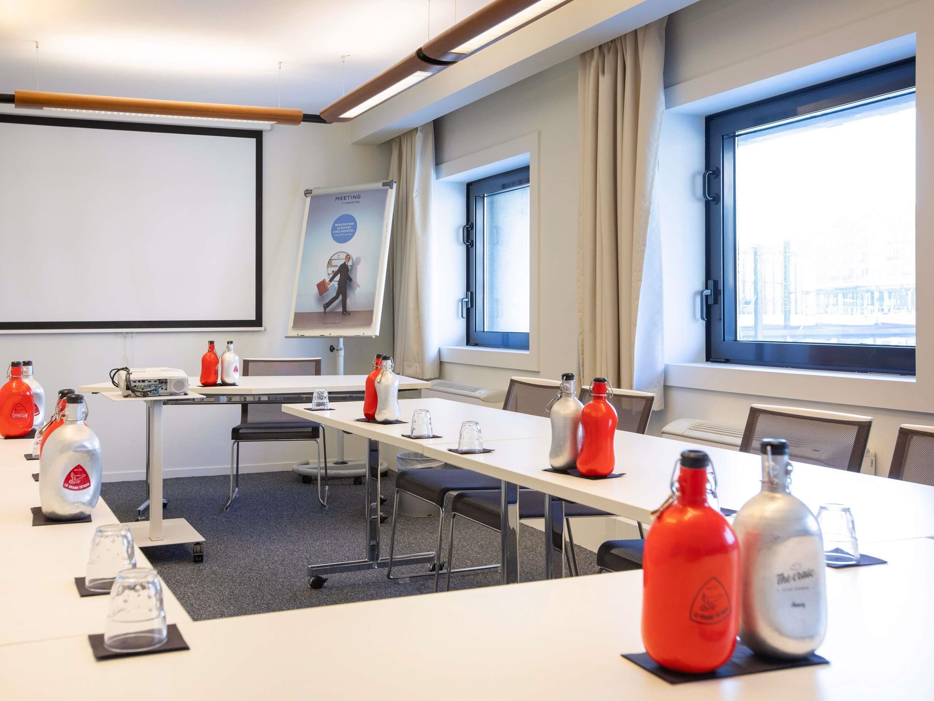 Ein Konferenzraum mit einem langen Tisch, Stühlen, einem Projektor und einer Präsentationsleinwand.