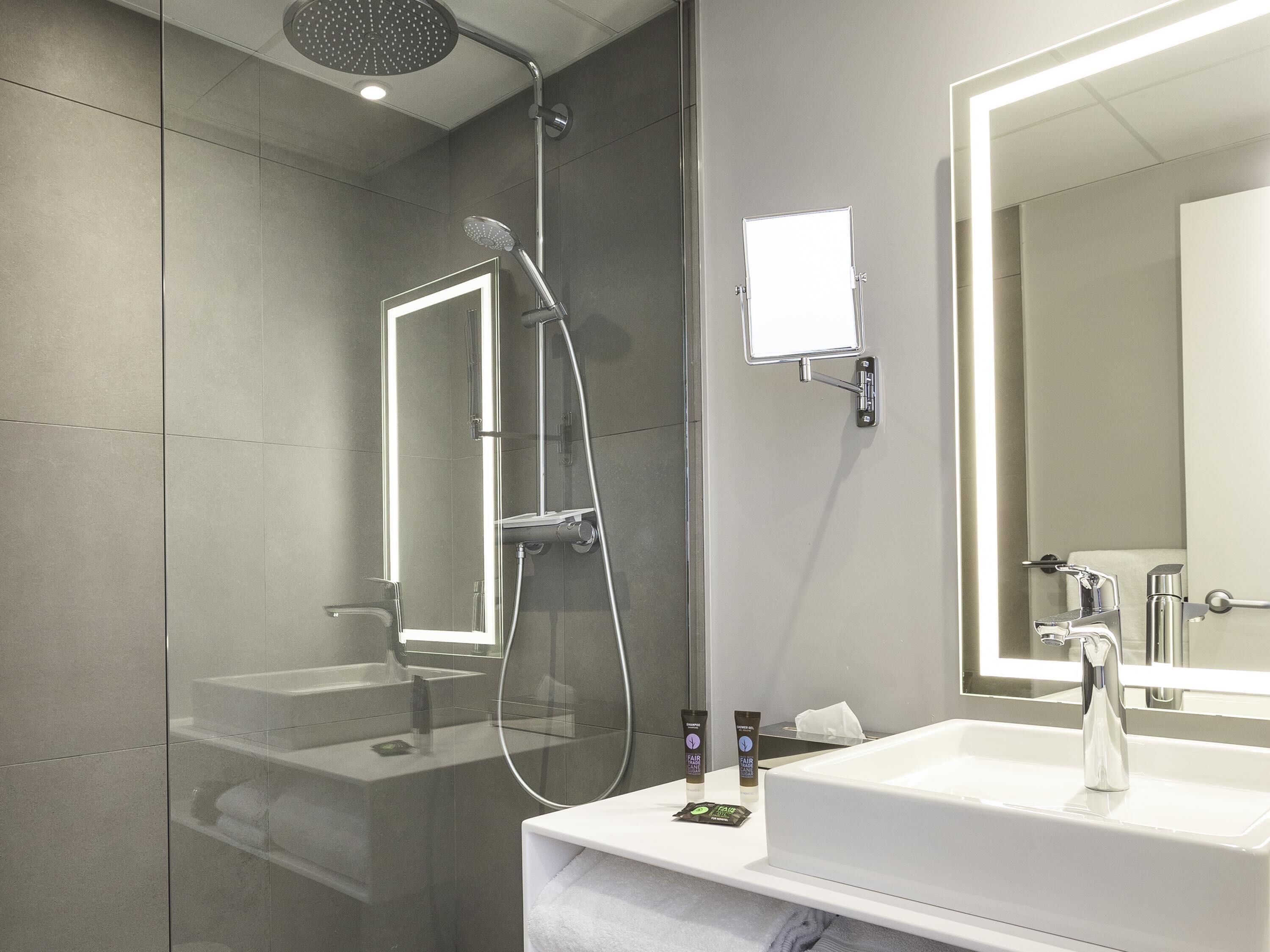 A modern bathroom with a glass-enclosed shower, a large mirror, and a white sink.