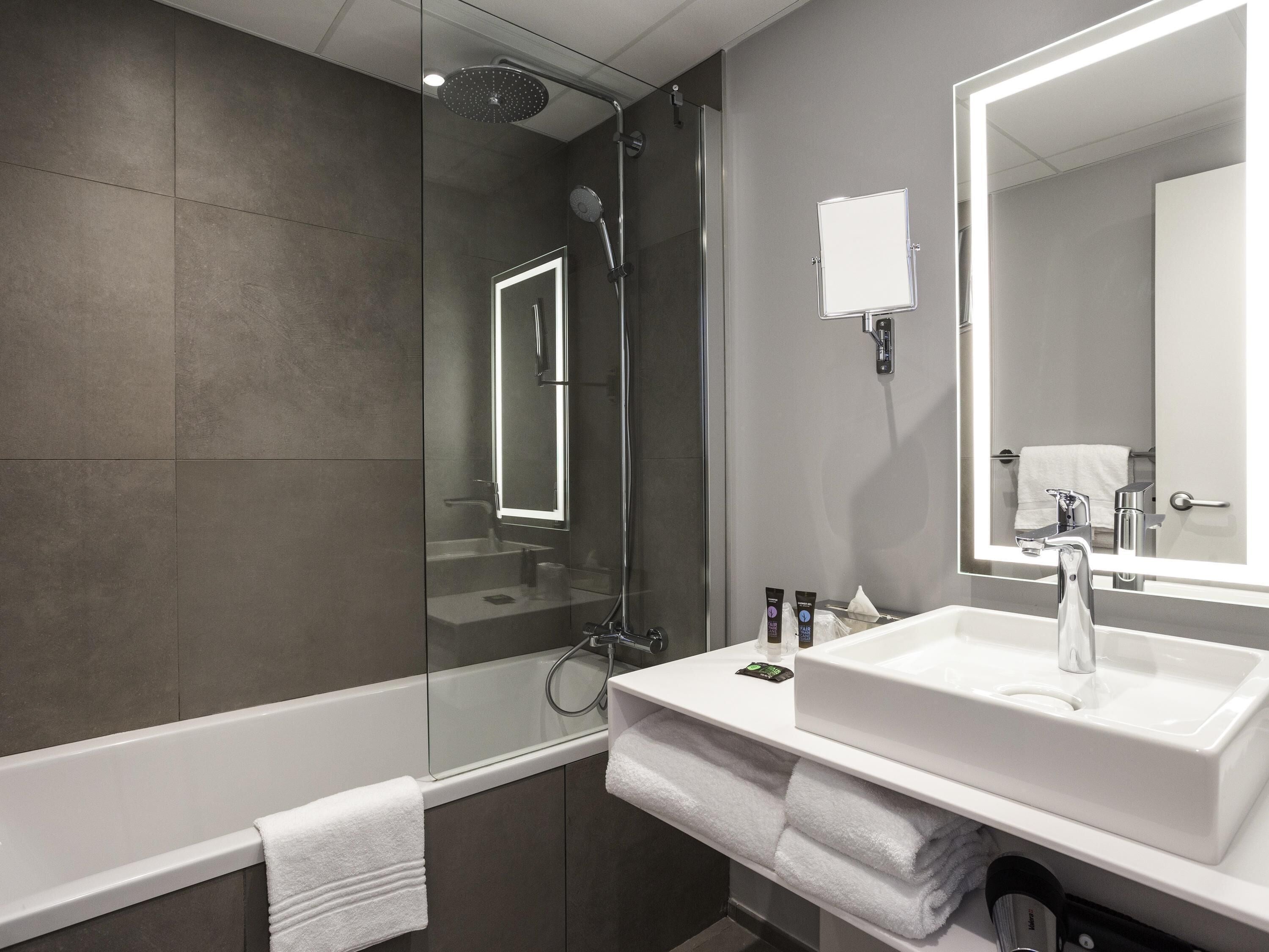 Une salle de bain moderne avec une douche à parois de verre, un grand miroir et un lavabo blanc avec un meuble-vasque.