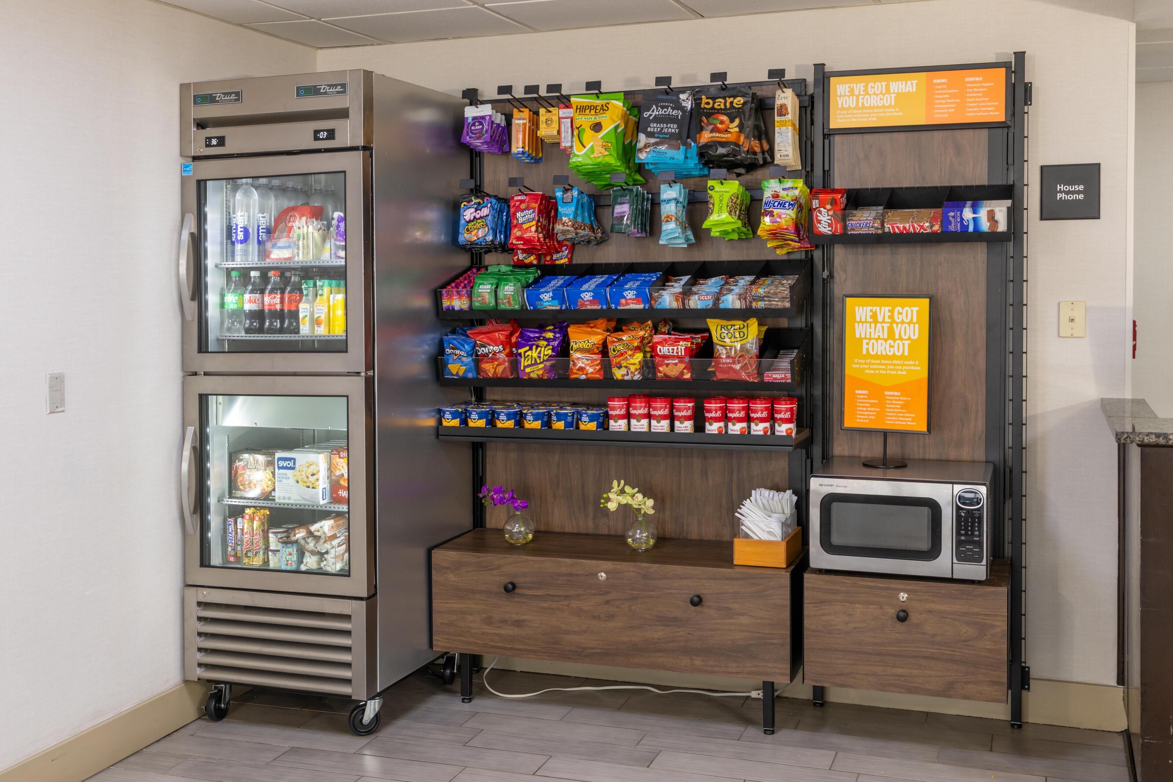 Máquina automática de snacks e bebidas, micro-ondas e placa com a mensagem 'Temos o que você esqueceu'.