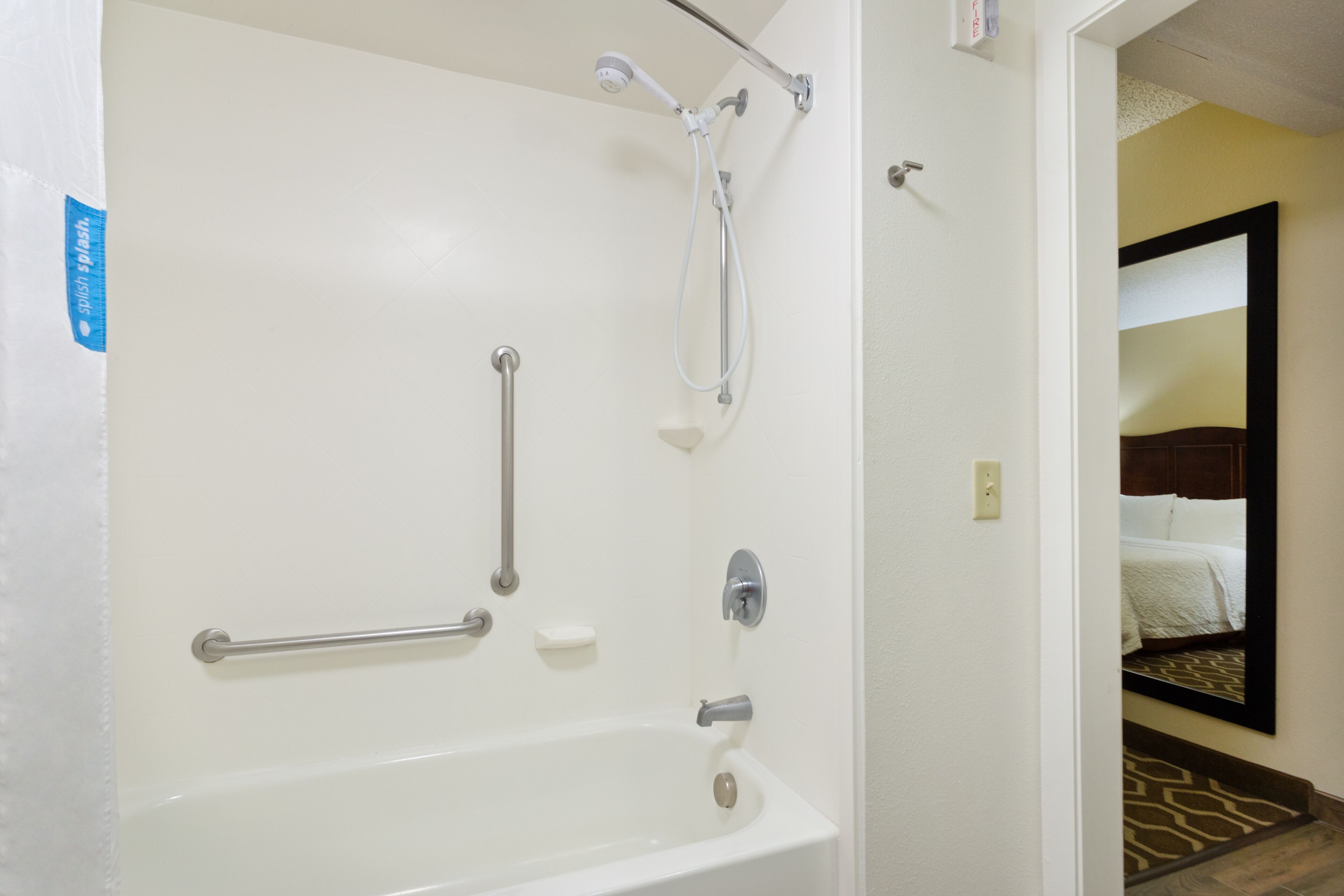 A bathroom with a bathtub, grab bars, a showerhead, and a towel rack.