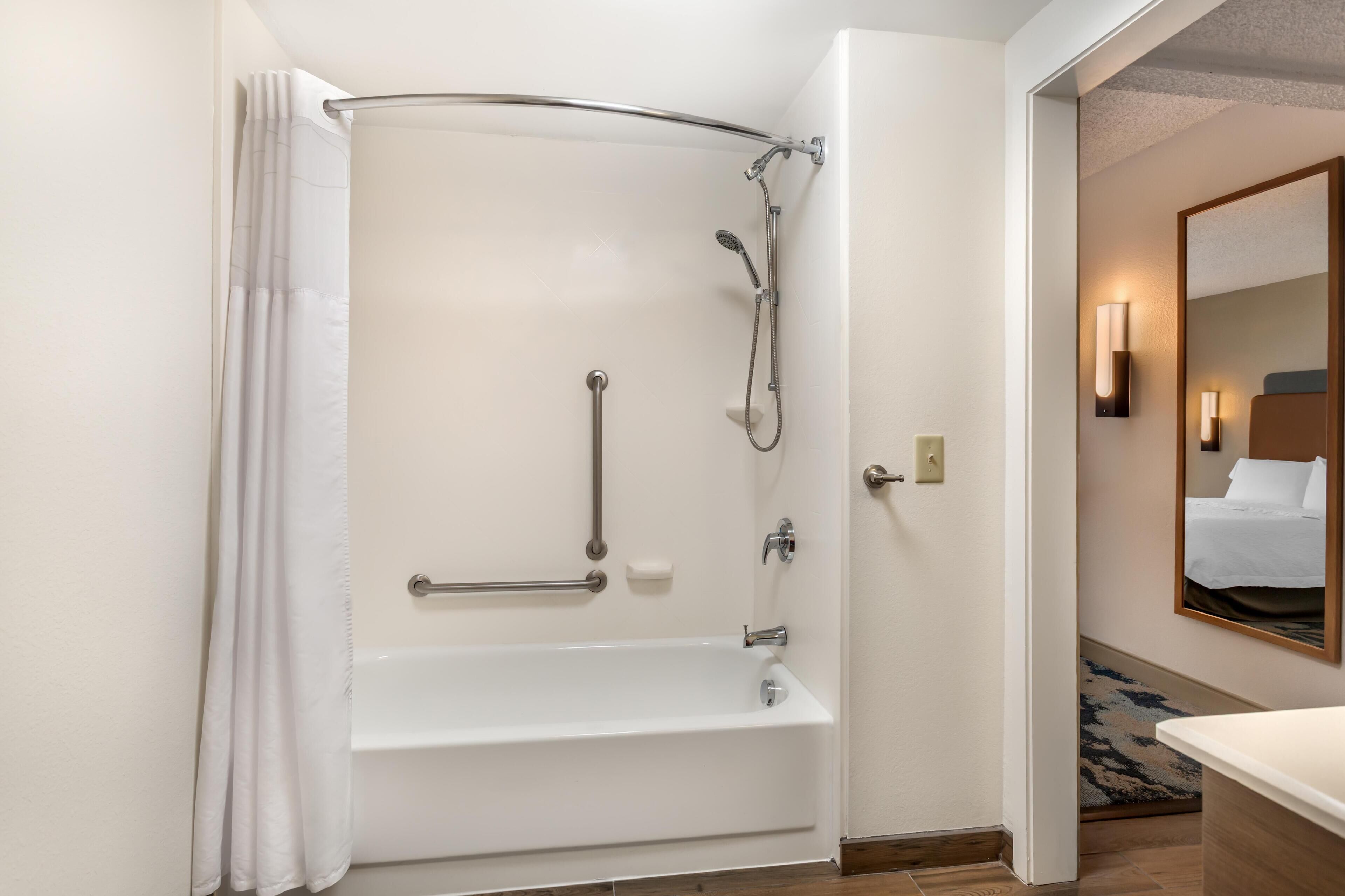 Ein Badezimmer mit Badewanne, Dusche, Haltegriffen und einem Spiegel.