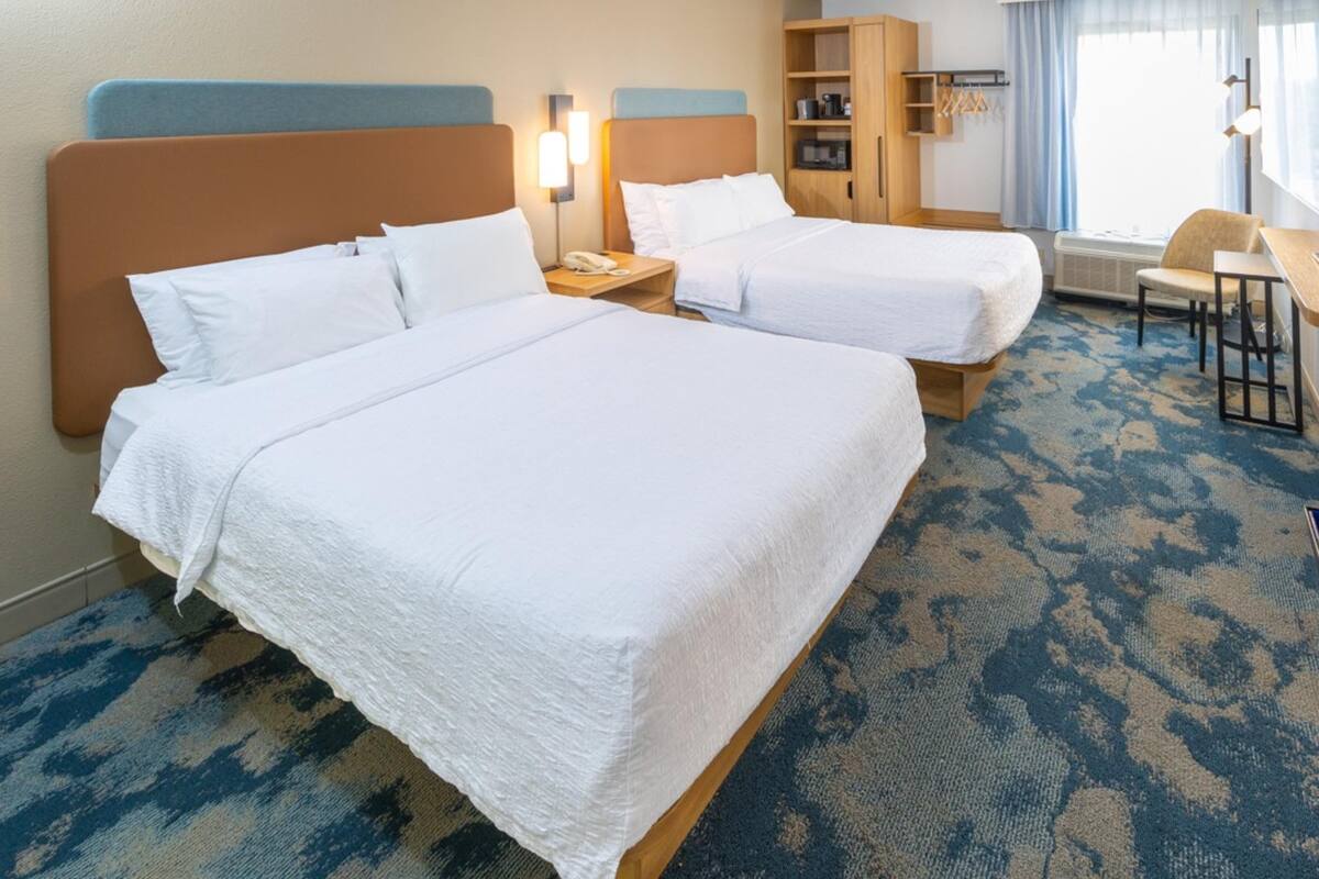 Een hotelkamer met twee bedden, een bureau, een stoel, een kledingkast en een raam met gordijnen.