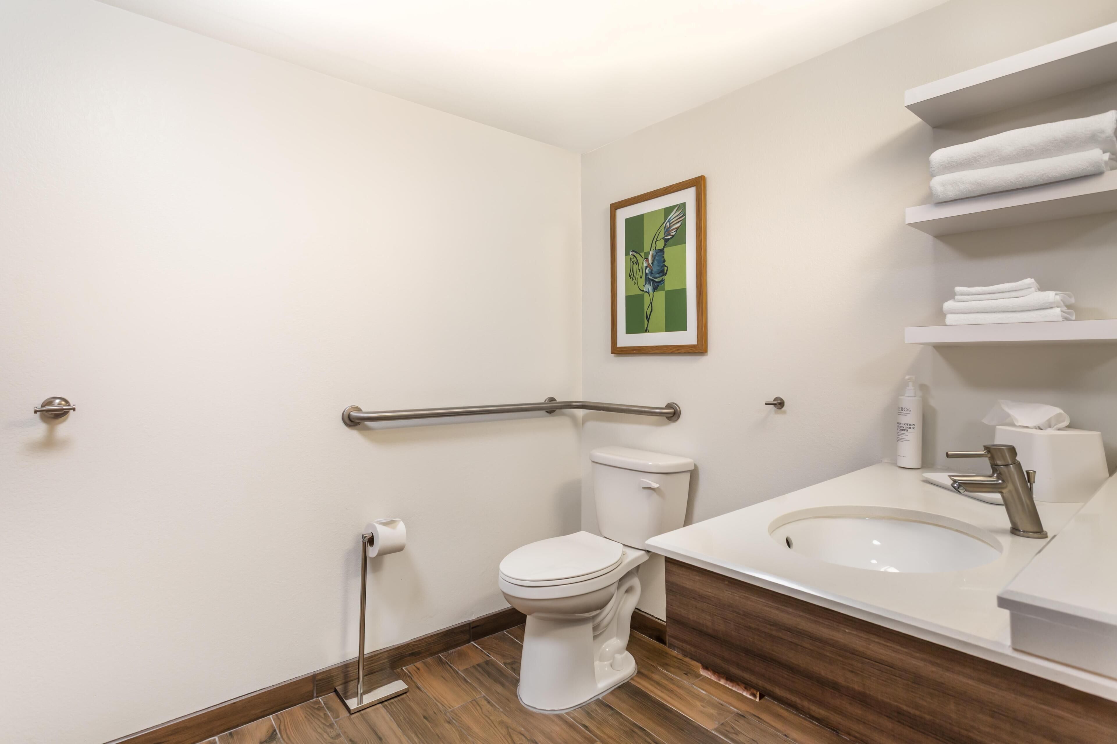 A modern bathroom with a toilet, sink, and handrail.