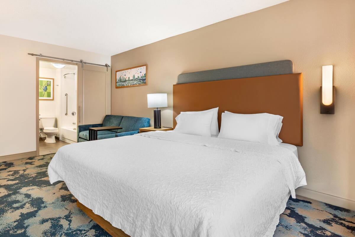 Een hotelkamer met een groot bed, een bureau, een stoel, een lamp en een schilderij aan de muur.