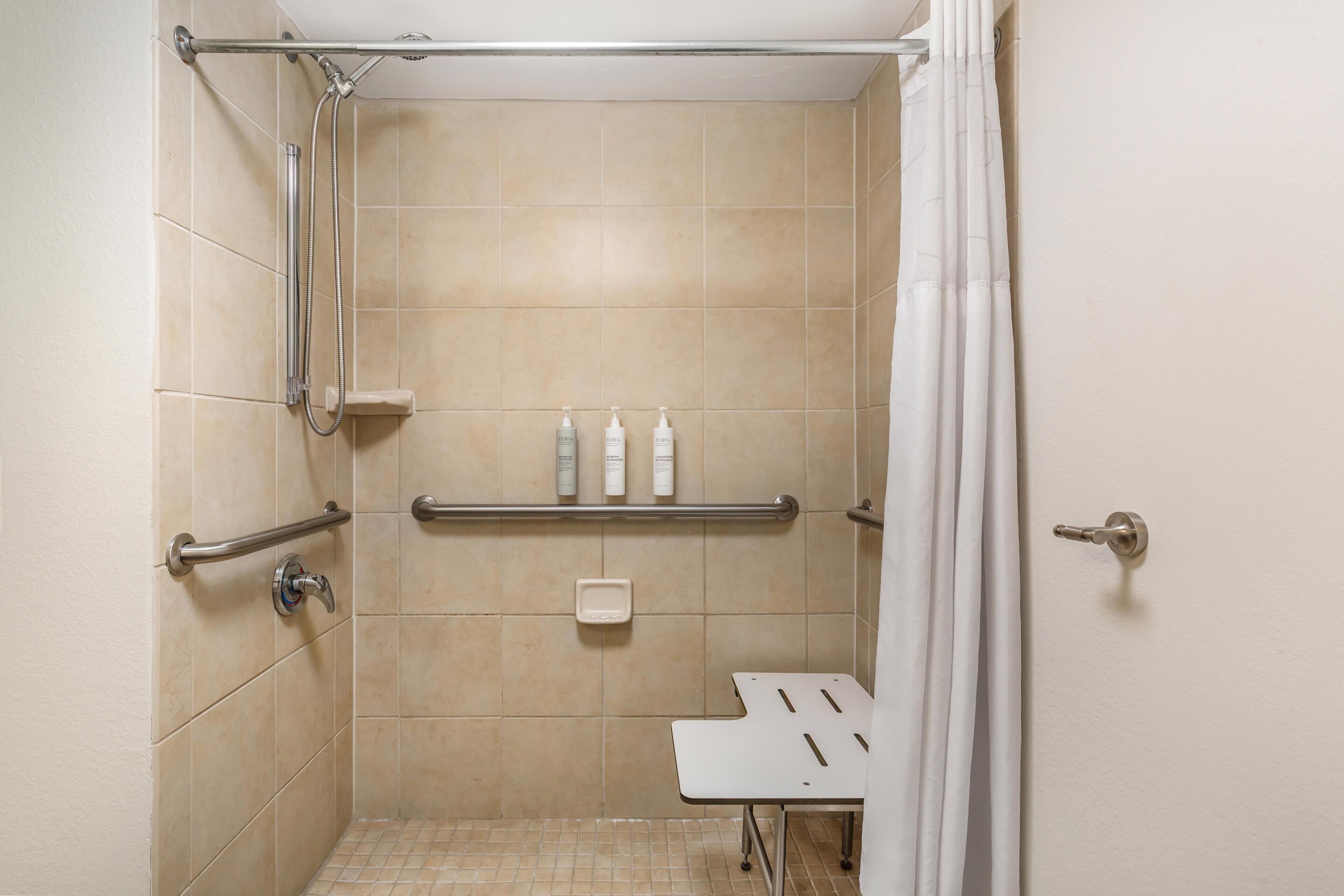 Une douche équipée de barres d’appui, une étagère avec des articles de toilette et une porte blanche.