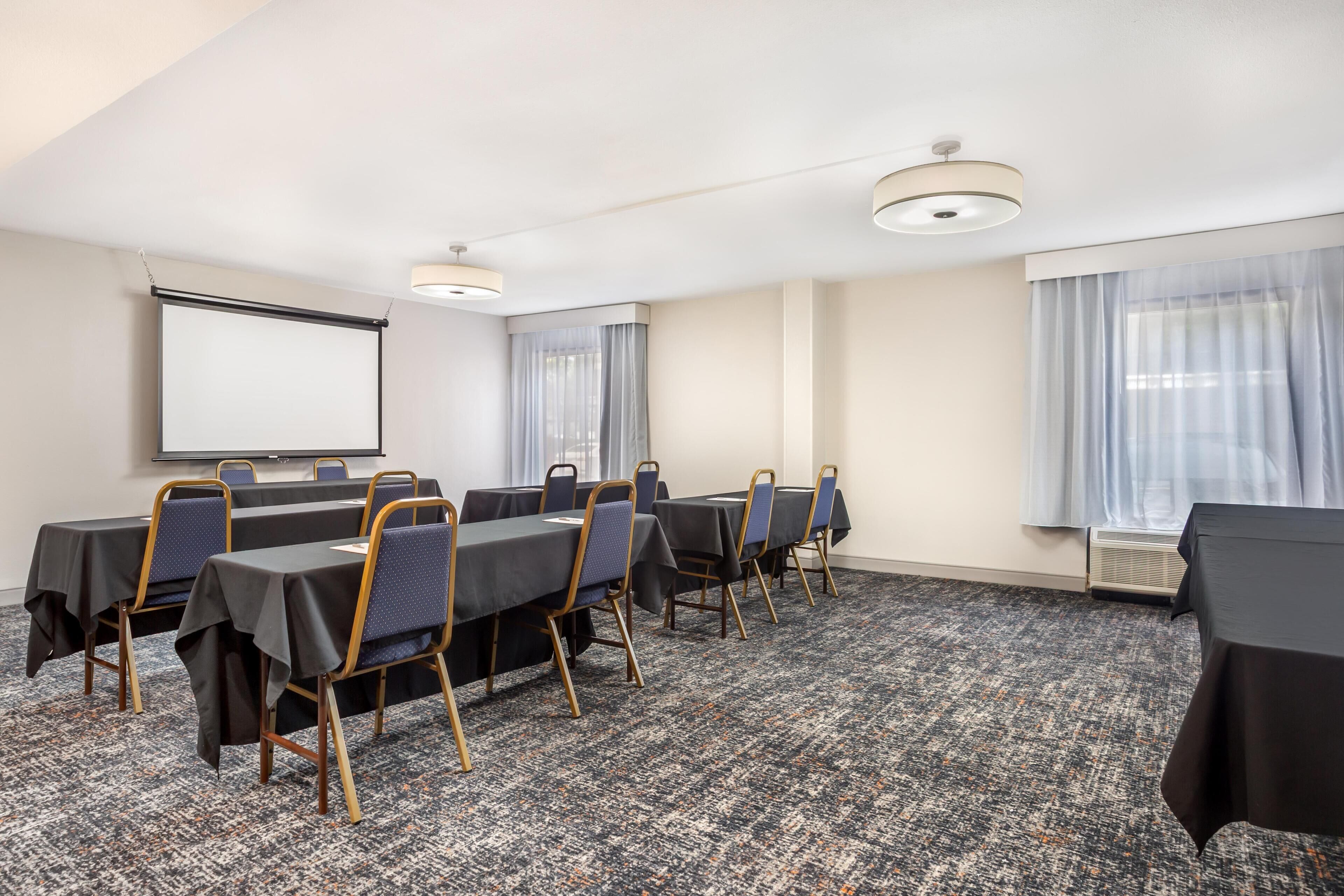 A conference room with a projector screen, tables, chairs, and a carpeted floor.