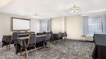 Un salón de conferencias con una pantalla de proyector, mesas, sillas y suelo alfombrado.