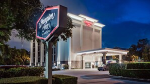Een Hampton Inn by Hilton hotel met een groot verlicht bord, een goed verlichte entree en een parkeerplaats.
