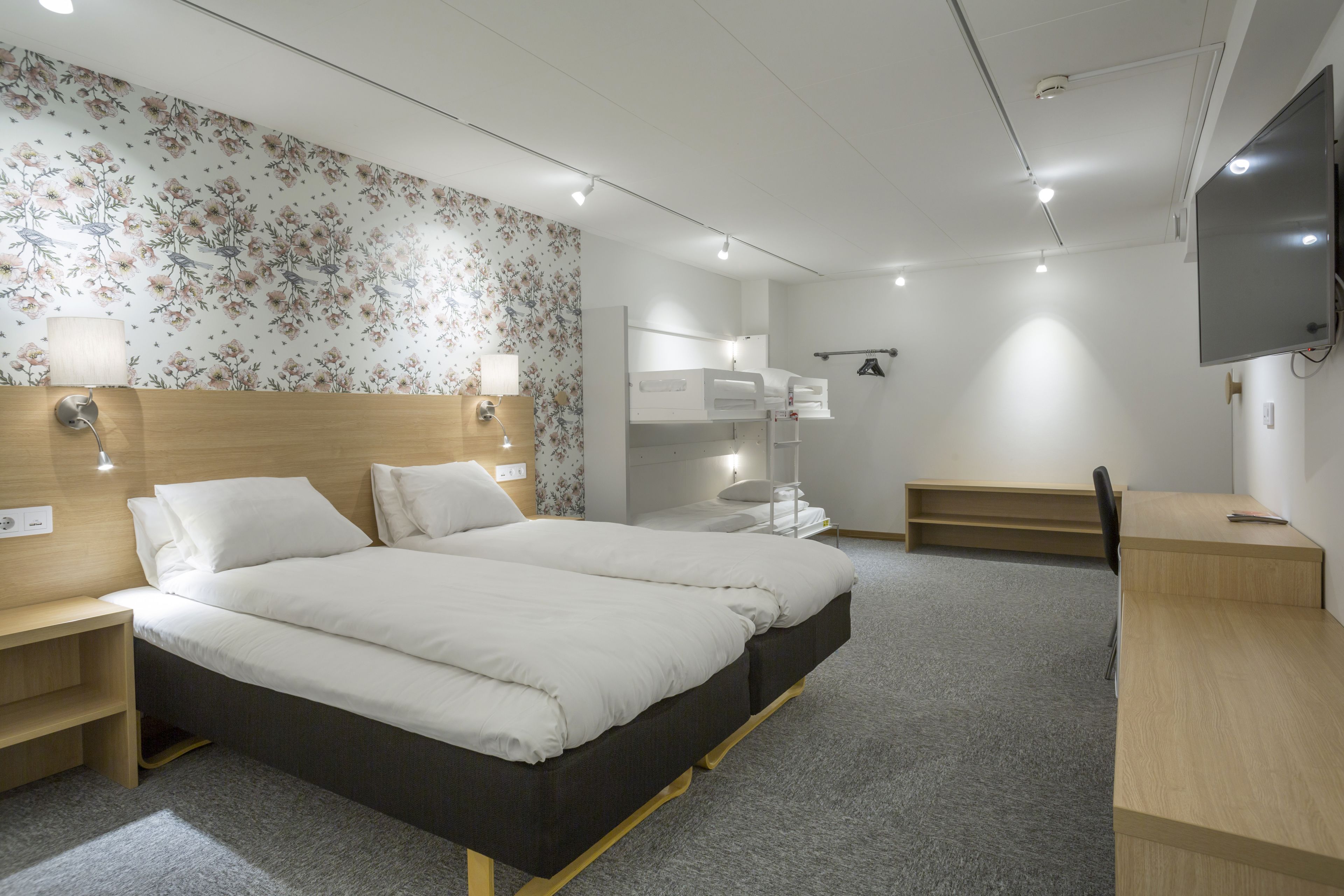 A modern hotel room with a large bed, bedside tables, a desk, a TV, and a wardrobe.