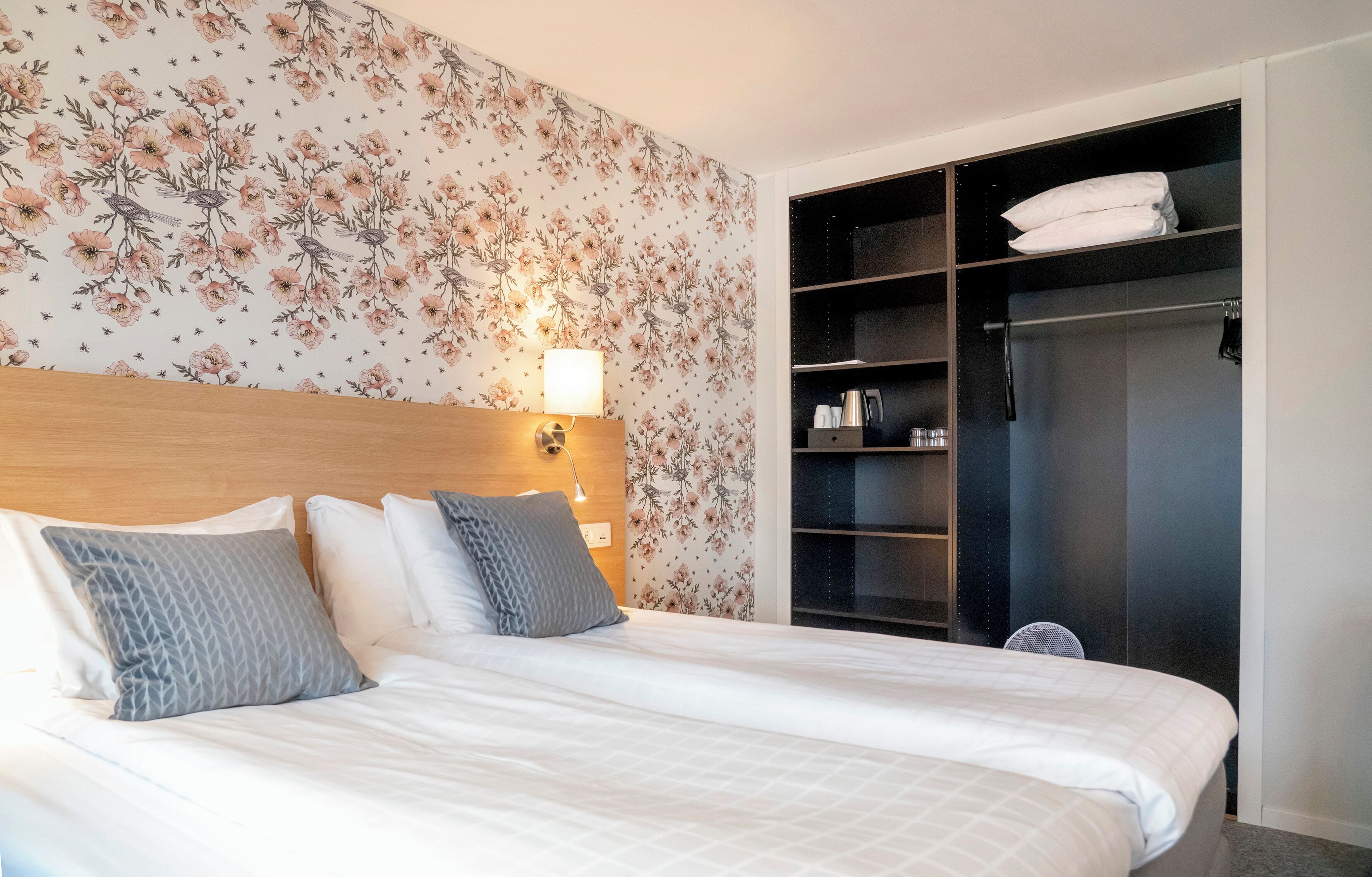 A hotel room with a bed, a nightstand, a wall-mounted lamp, and a built-in wardrobe with shelves.