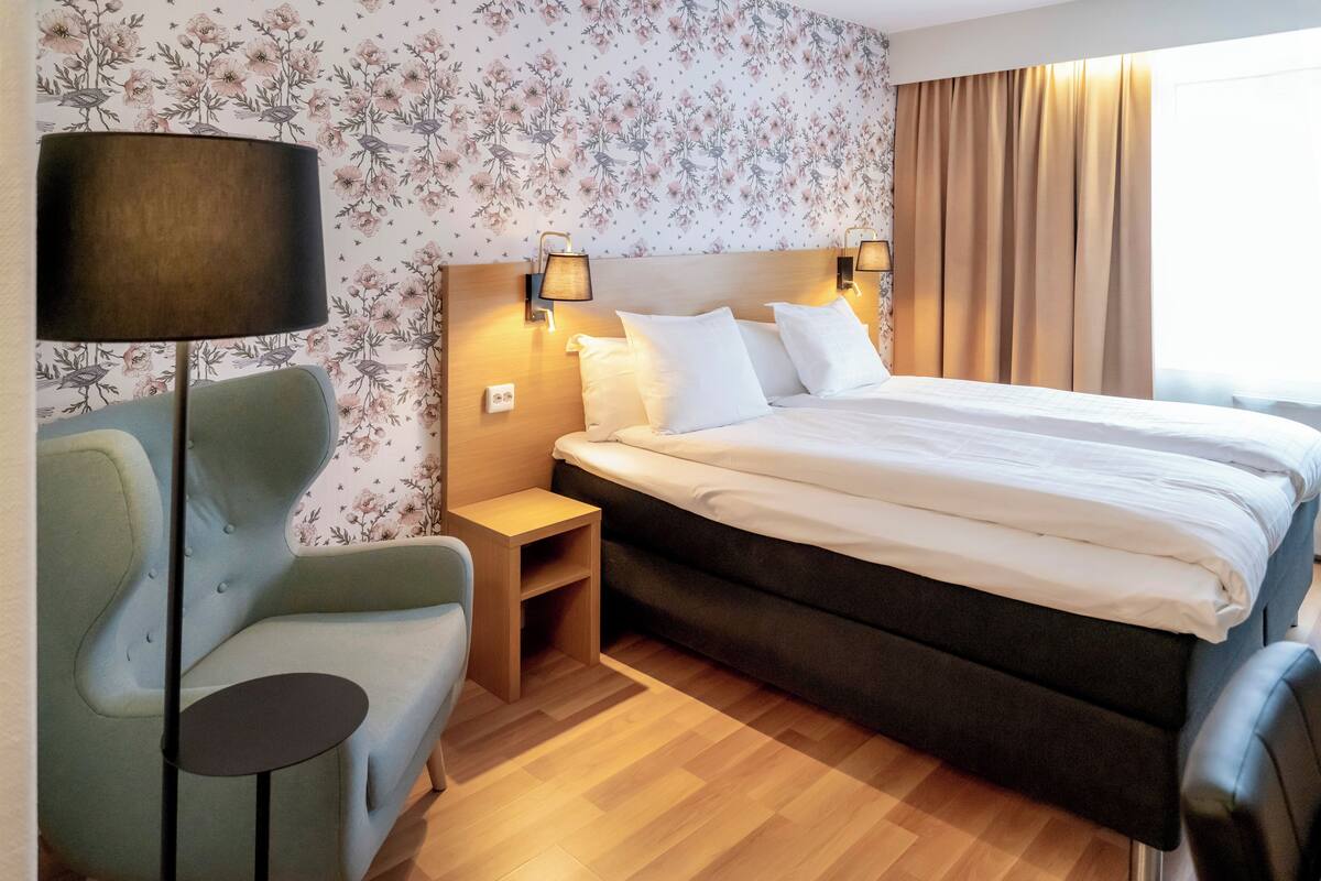A hotel room with a bed, nightstands, a lamp, a chair, and a small table.