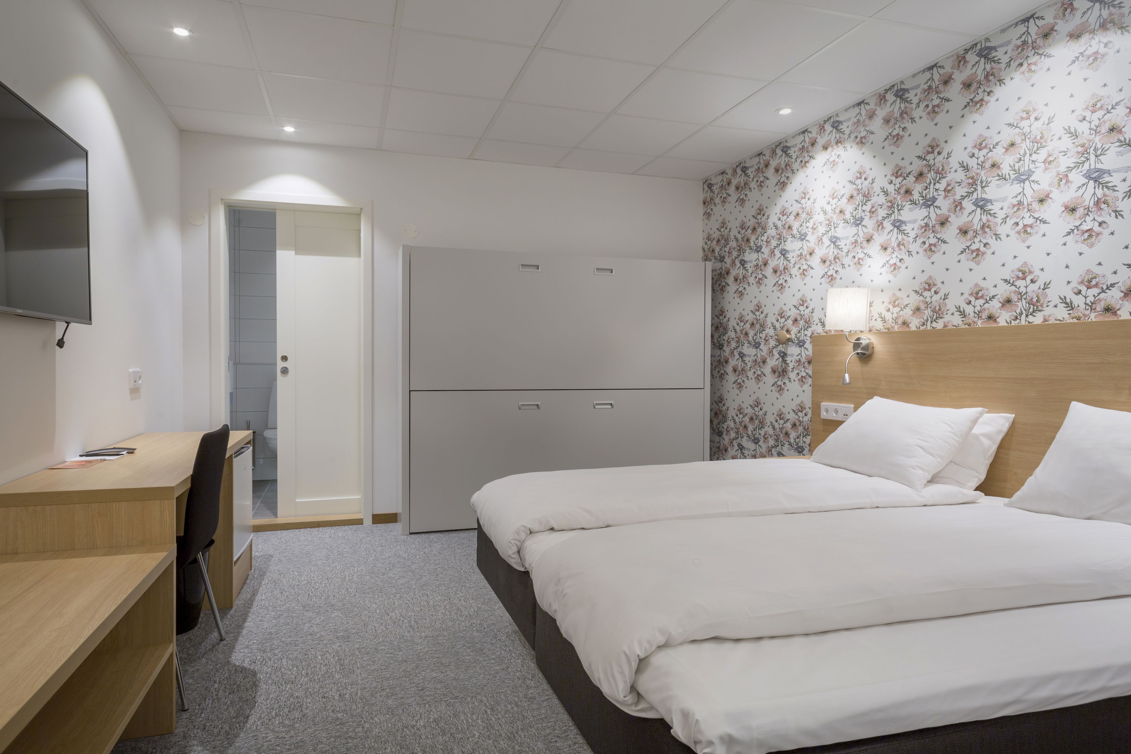 Habitación de hotel con cama, escritorio, silla, televisión y armario.