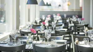 A restaurant with multiple tables set for dining, each with a wine glass and a flower centerpiece. - First Hotel Dragonen (Umea)