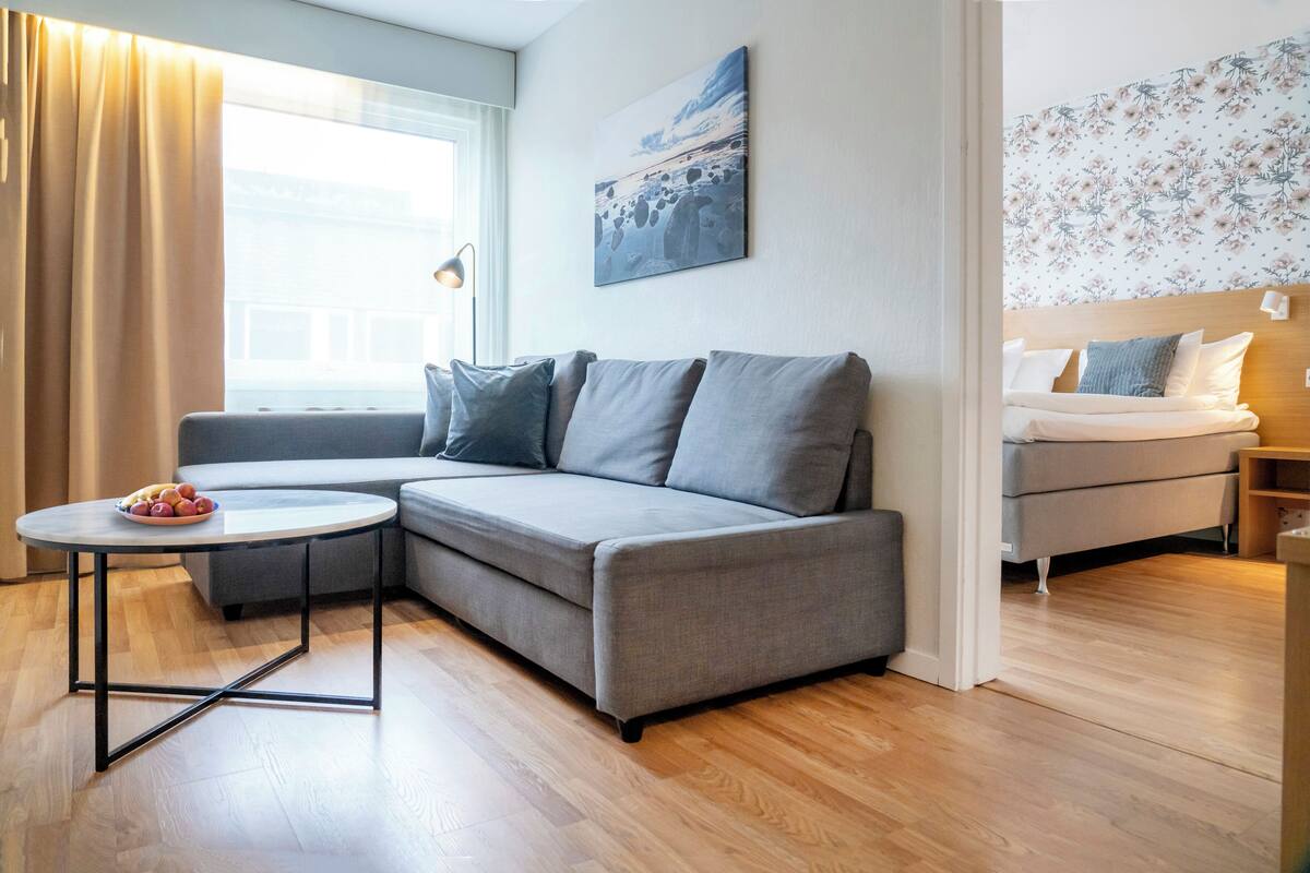 A modern living room with a grey sofa, a round coffee table, and a bed with a floral headboard.