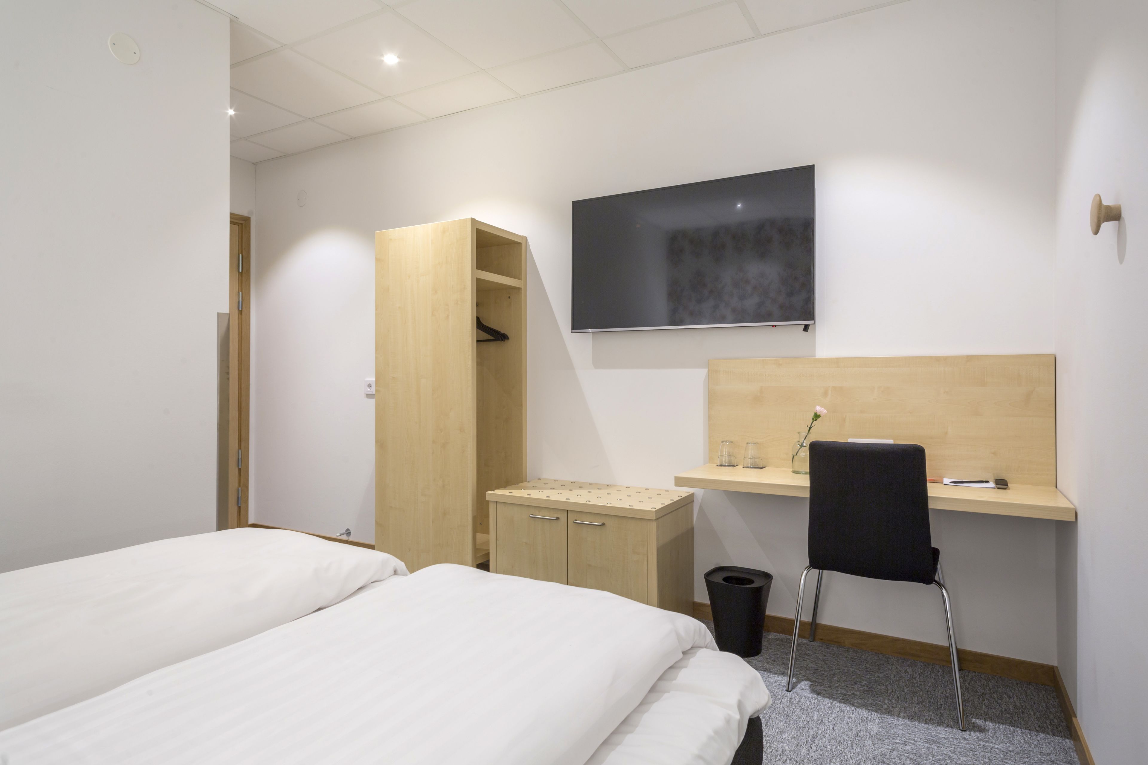 A hotel room with two beds, a wooden desk, a chair, a TV, and a wardrobe.