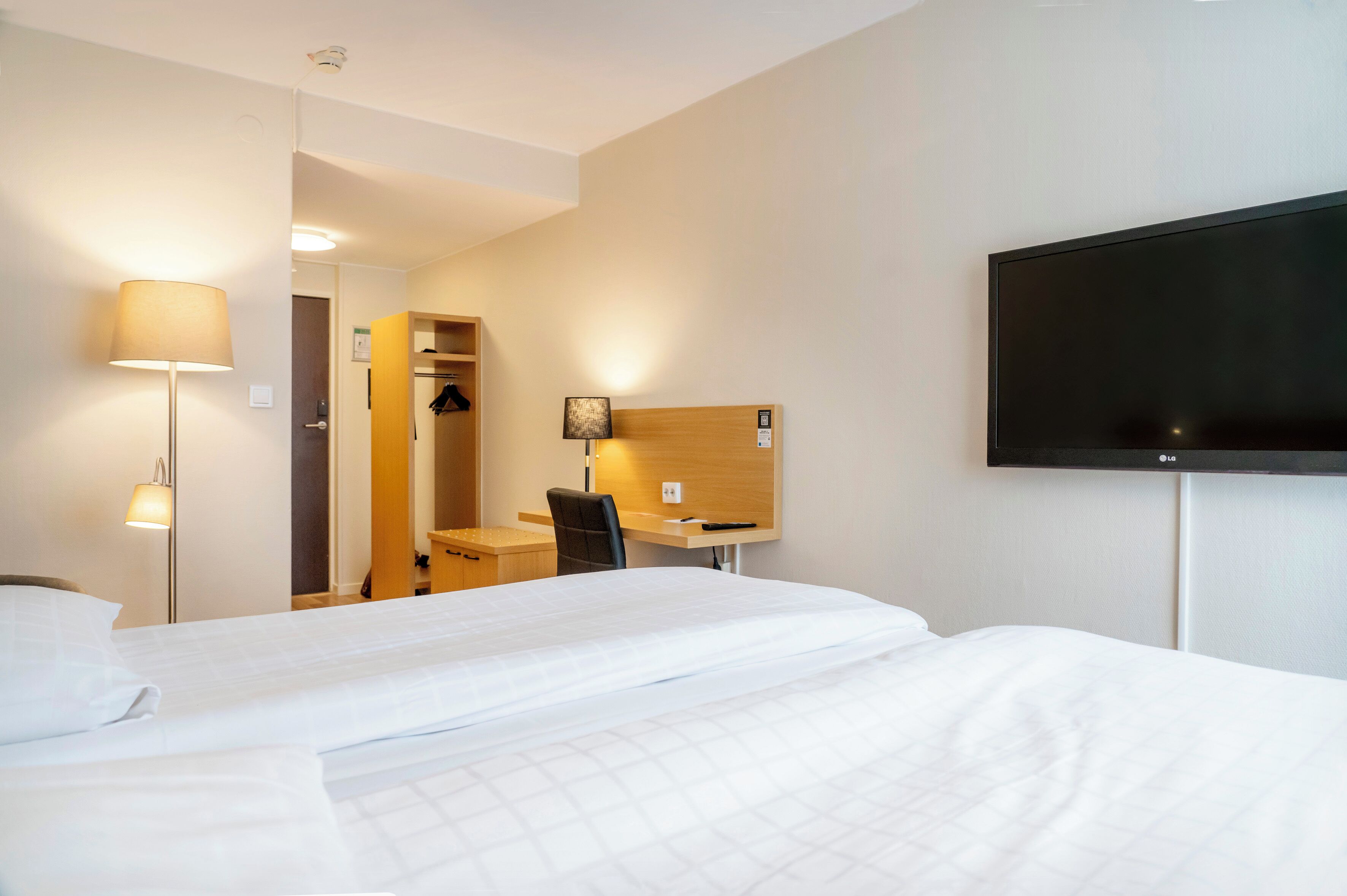 Ein Hotelzimmer mit einem Bett, einem Schreibtisch, einem Sessel, einem Fernseher und einem Kleiderschrank.