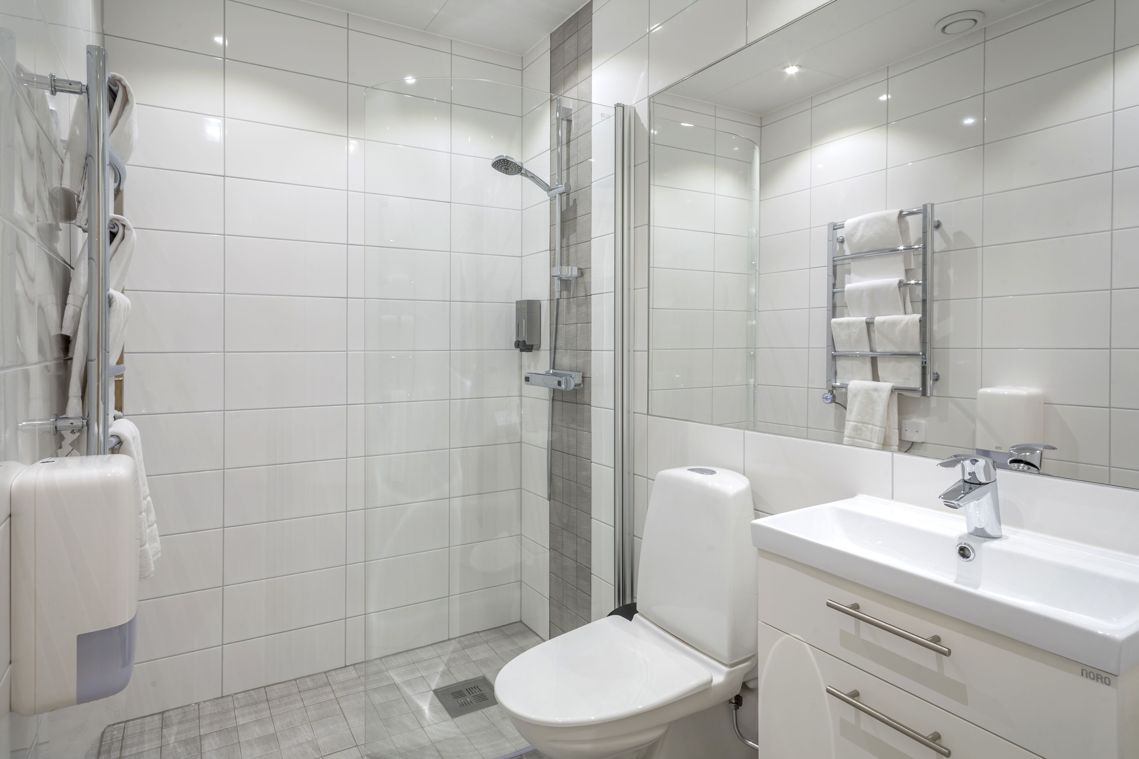 A modern bathroom with white tiles, a glass shower enclosure, a white sink, and a mirror.