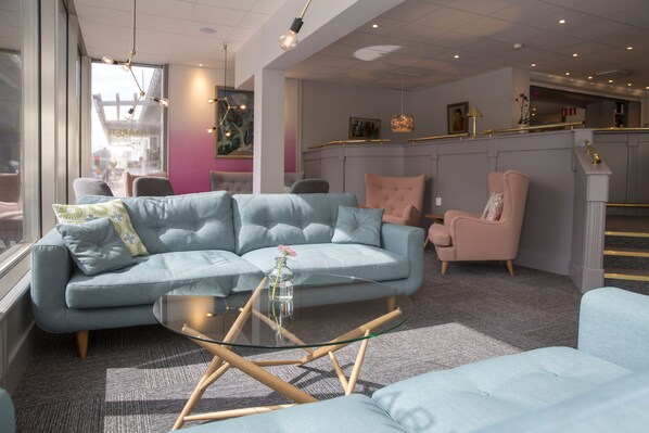 A modern living room with a grey sofa, a glass coffee table, and a pink armchair.