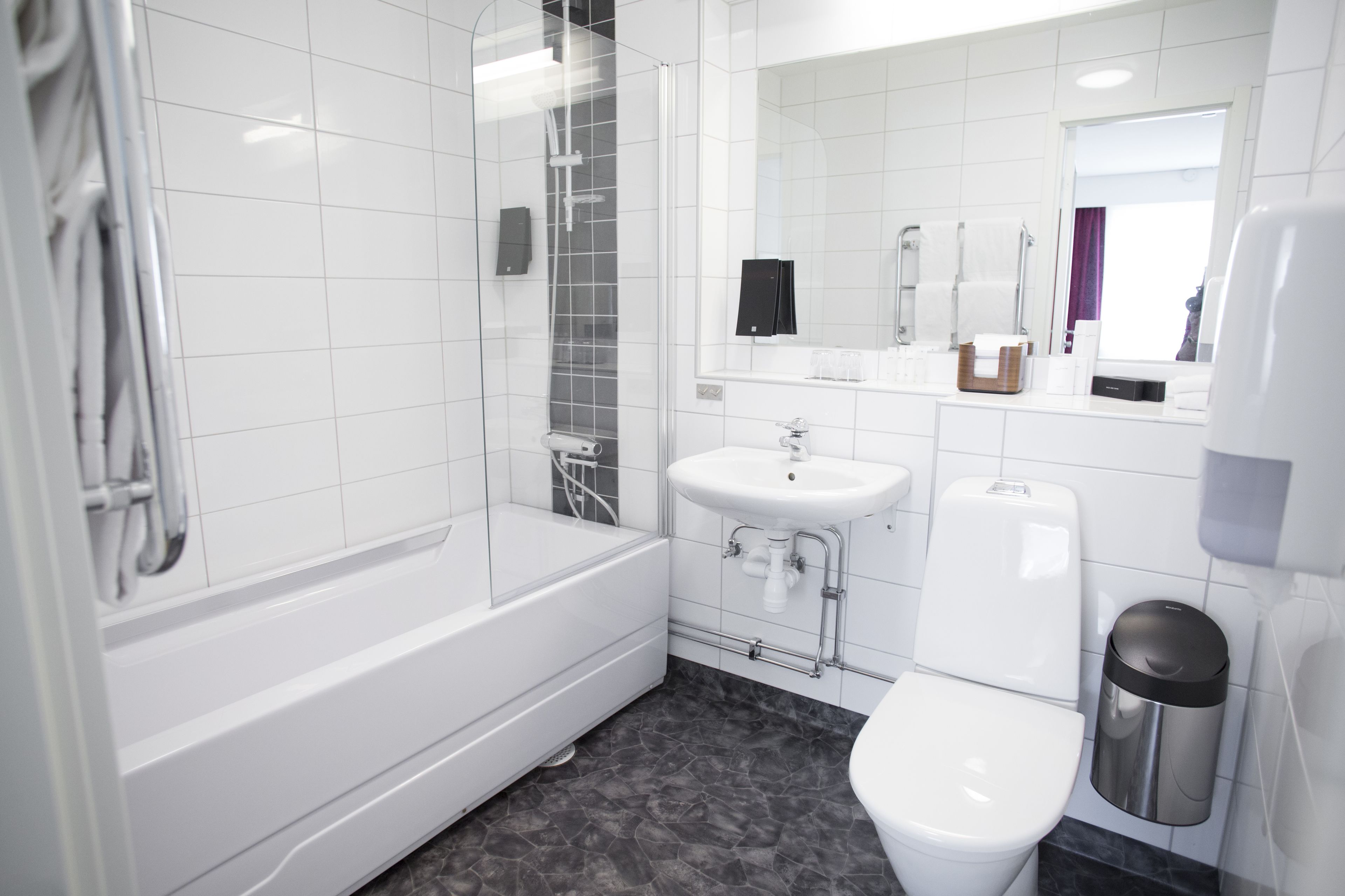 A modern bathroom with a glass-enclosed shower, a white sink, a toilet, and a trash can.