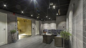 A modern indoor space with a dark ceiling, grey tiled walls, and a central seating area with a sofa and a coffee table. - First Hotel Dragonen (Umea)