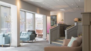 A modern hotel lobby with a staircase, seating areas, and large windows. - First Hotel Dragonen (Umea)