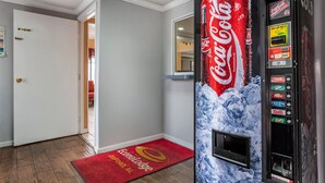 A Coca-Cola vending machine in a hotel lobby with a red carpet and a door leading to another room. - Econo Lodge Oxford near Choccolocco Park (Oxford)