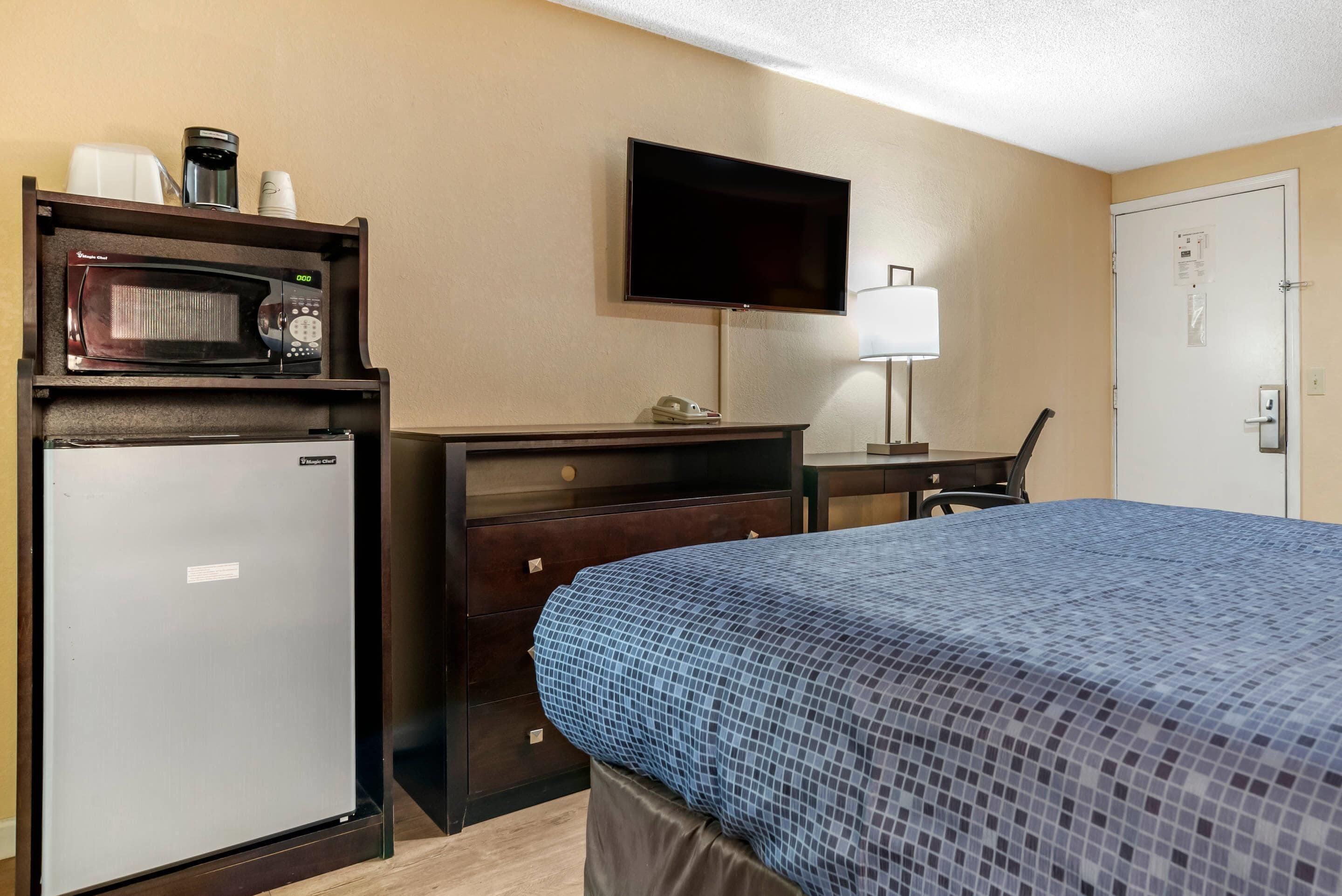 A hotel room with a bed, a desk with a chair, a television, a microwave, and a refrigerator.