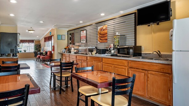 A hotel lobby with wooden flooring, a reception desk, a seating area with tables and chairs, a kitchen area with a microwave, and a television mounted on the wall. - Econo Lodge Oxford near Choccolocco Park (Oxford)