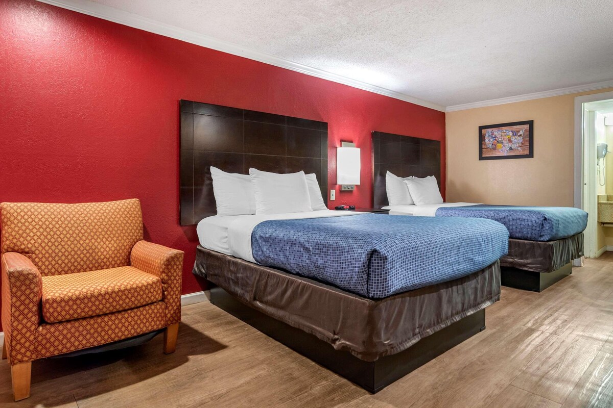 Een hotelkamer met een rode muur, twee bedden met blauw beddengoed, een houten stoel en een kaart aan de muur.