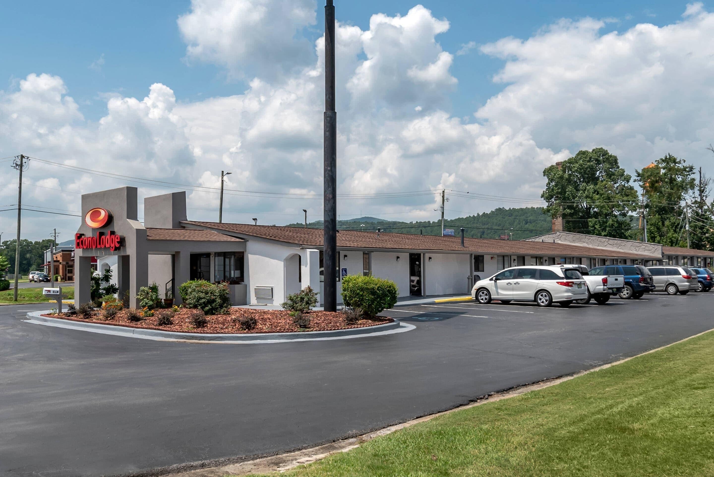 A motel with a central sign, a parking lot, and a grassy area.