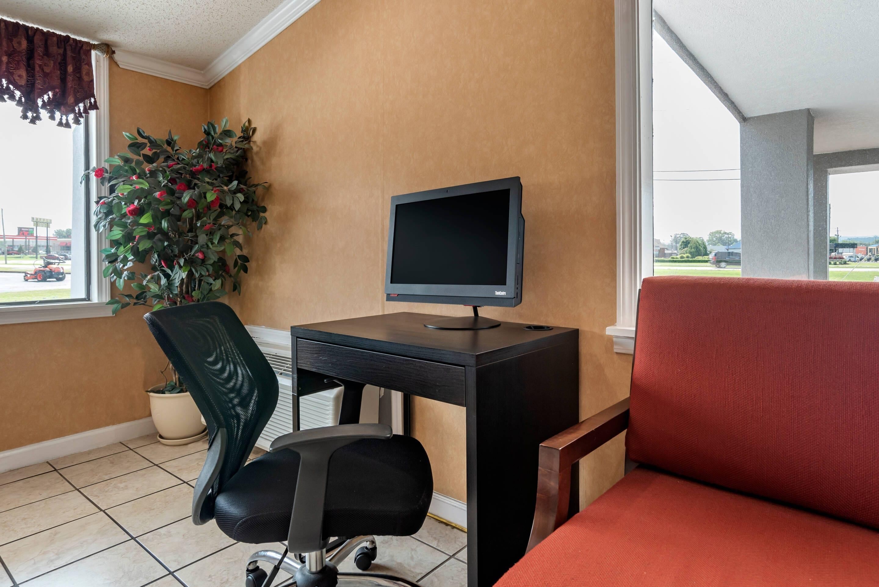 A room with a desk, computer, chair, potted plant, and a view of the outside.