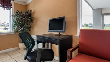 A room with a desk, computer, chair, potted plant, and a view of the outside.