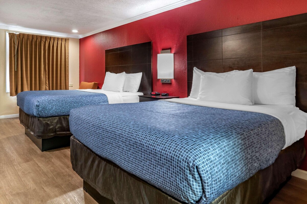 Hotelkamer met twee bedden, een rode accentmuur, een houten hoofdeinde en een nachtkastje met een lamp.