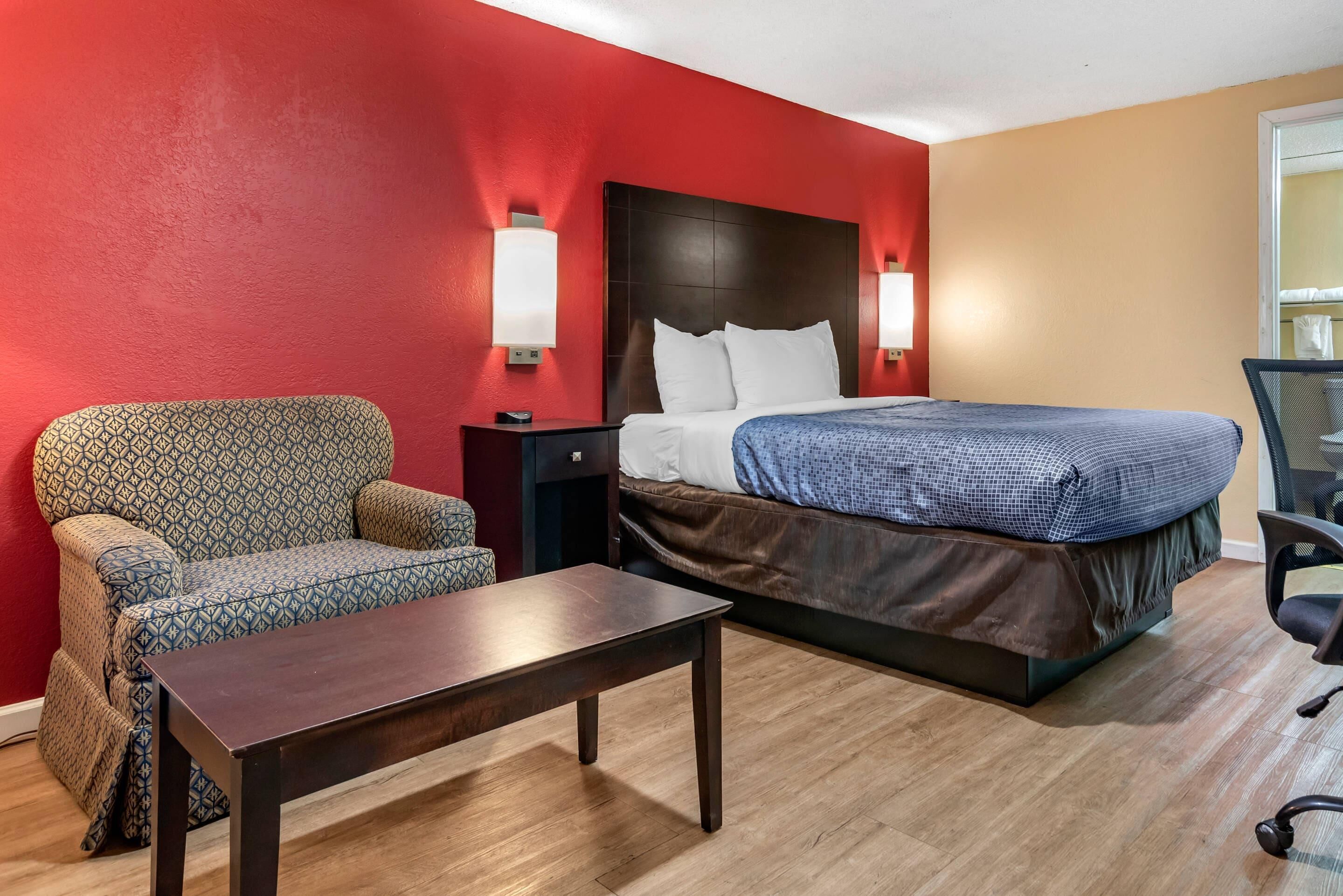 A hotel room with a bed, a sofa, a small table, and two wall-mounted lamps.