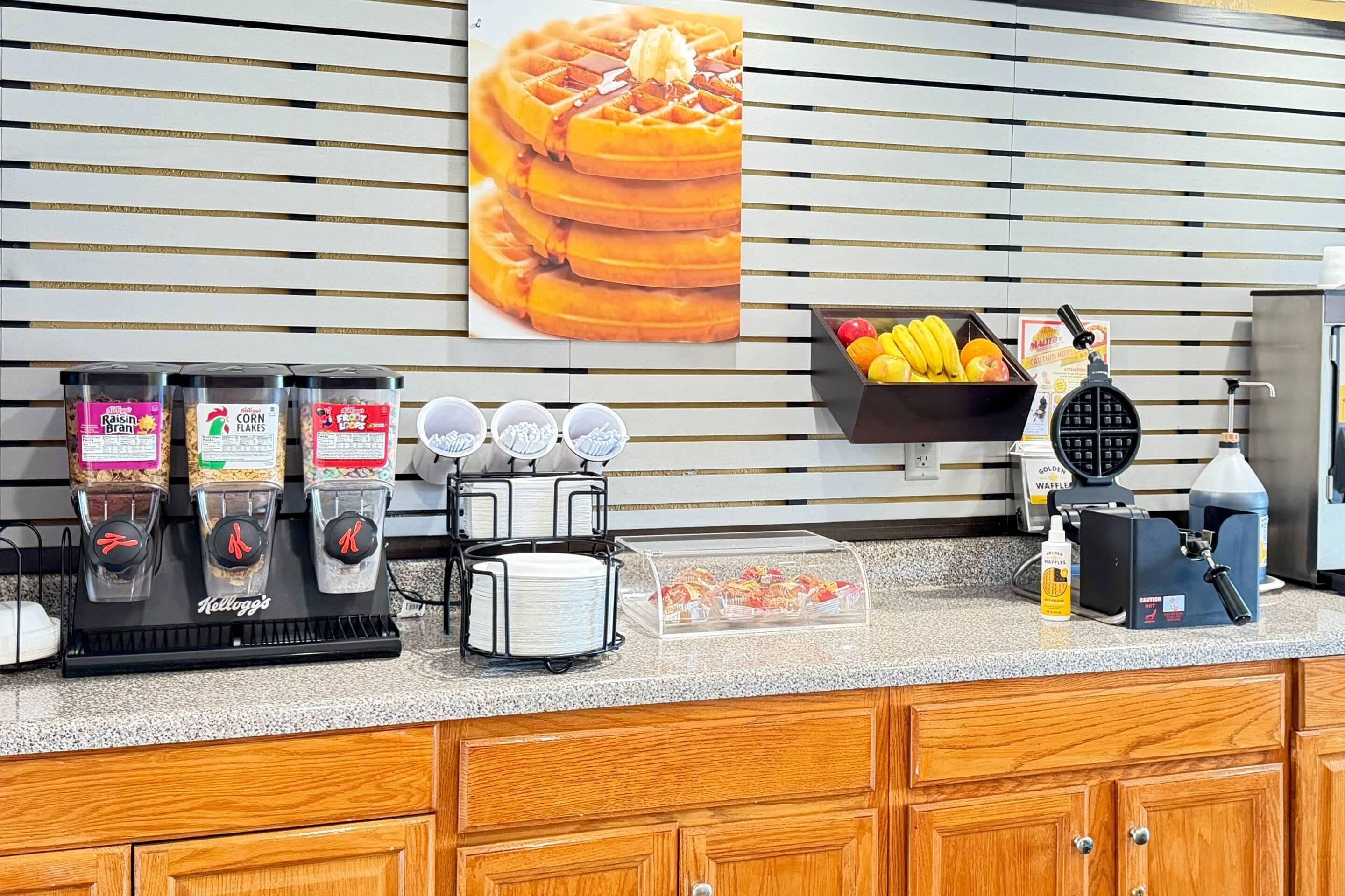 A breakfast bar with waffle makers, coffee machines, and a fruit display.