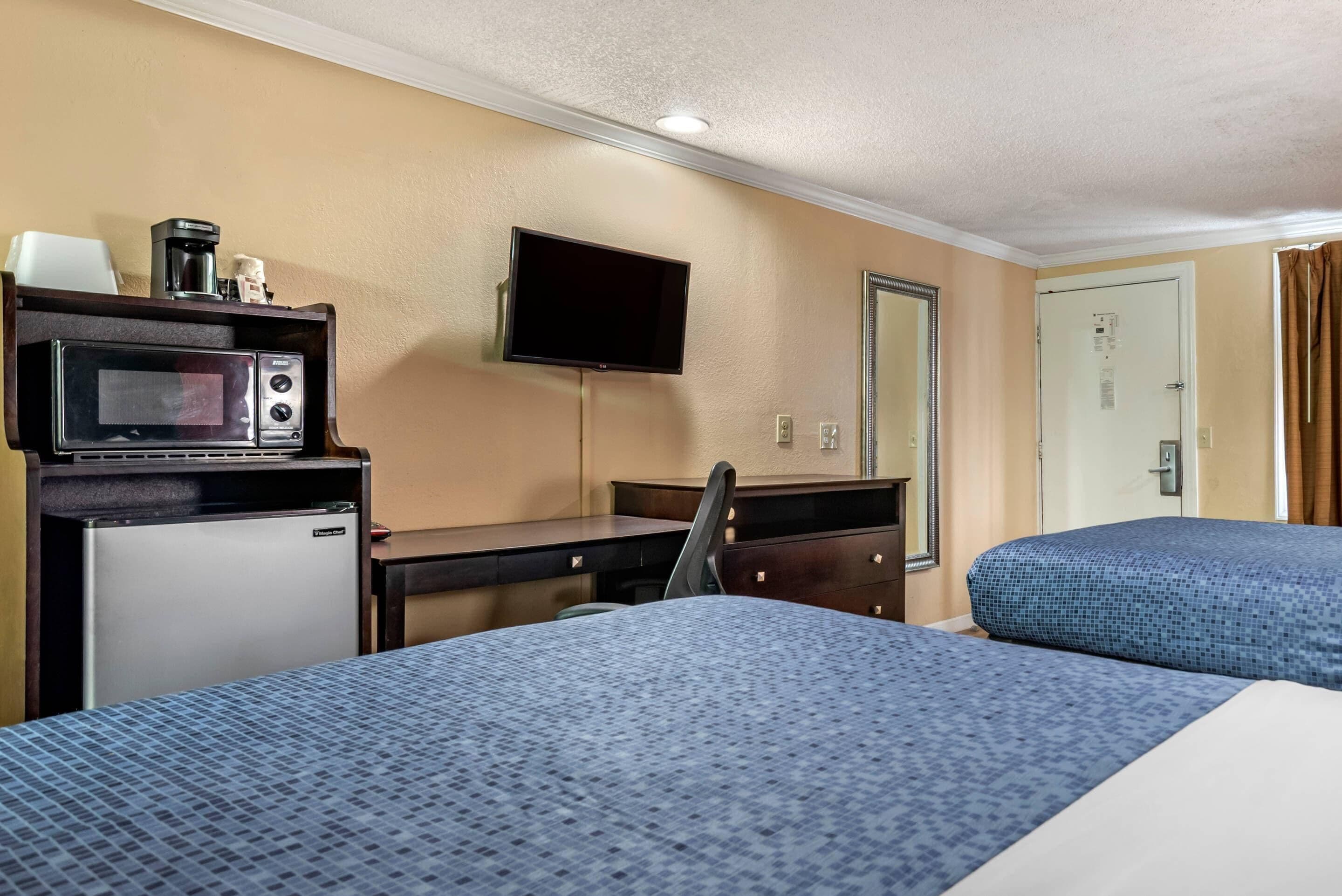 A hotel room with a bed, a desk with a microwave, a television, and a door.