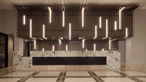 Un hall d’entrée moderne avec un comptoir de réception en marbre, un sol à motifs et un plafond orné de luminaires verticaux.