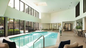 Une piscine intérieure moderne, dotée d’une paroi en verre, entourée de meubles en osier et comprenant un espace repas.