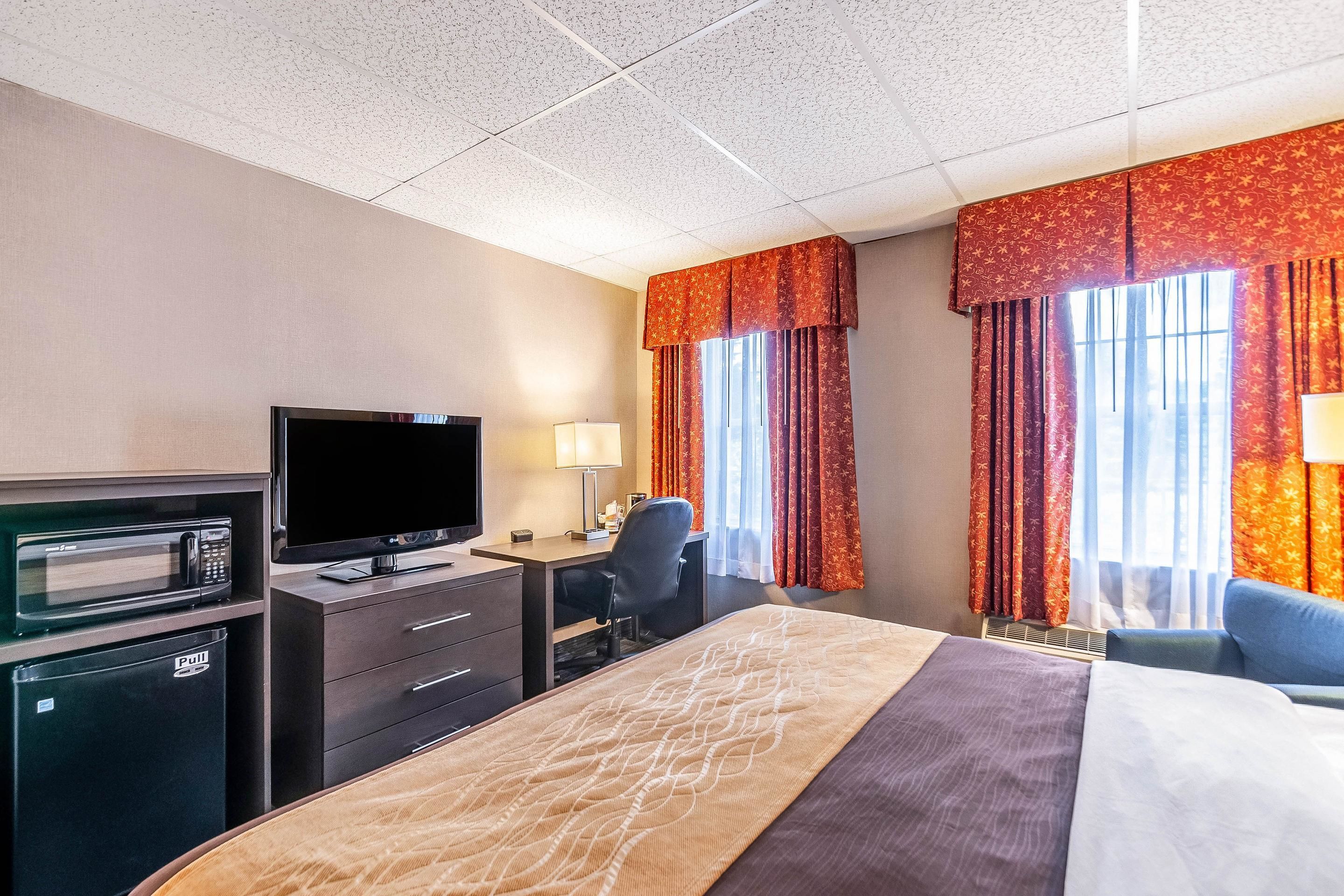 Quarto de hotel com cama, escrivaninha, televisão, micro-ondas e mini-geladeira.