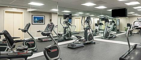 A gym with multiple cardio machines, mirrors, and a television on the wall.
