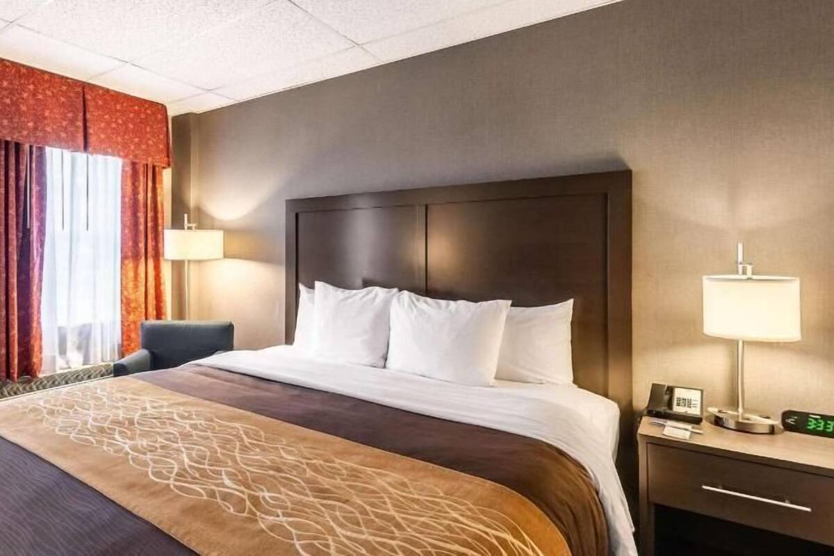 Hotellihuone, jossa on sänky, yöpöytä lampun kanssa, tuoli ja ikkuna, jossa on verhot.