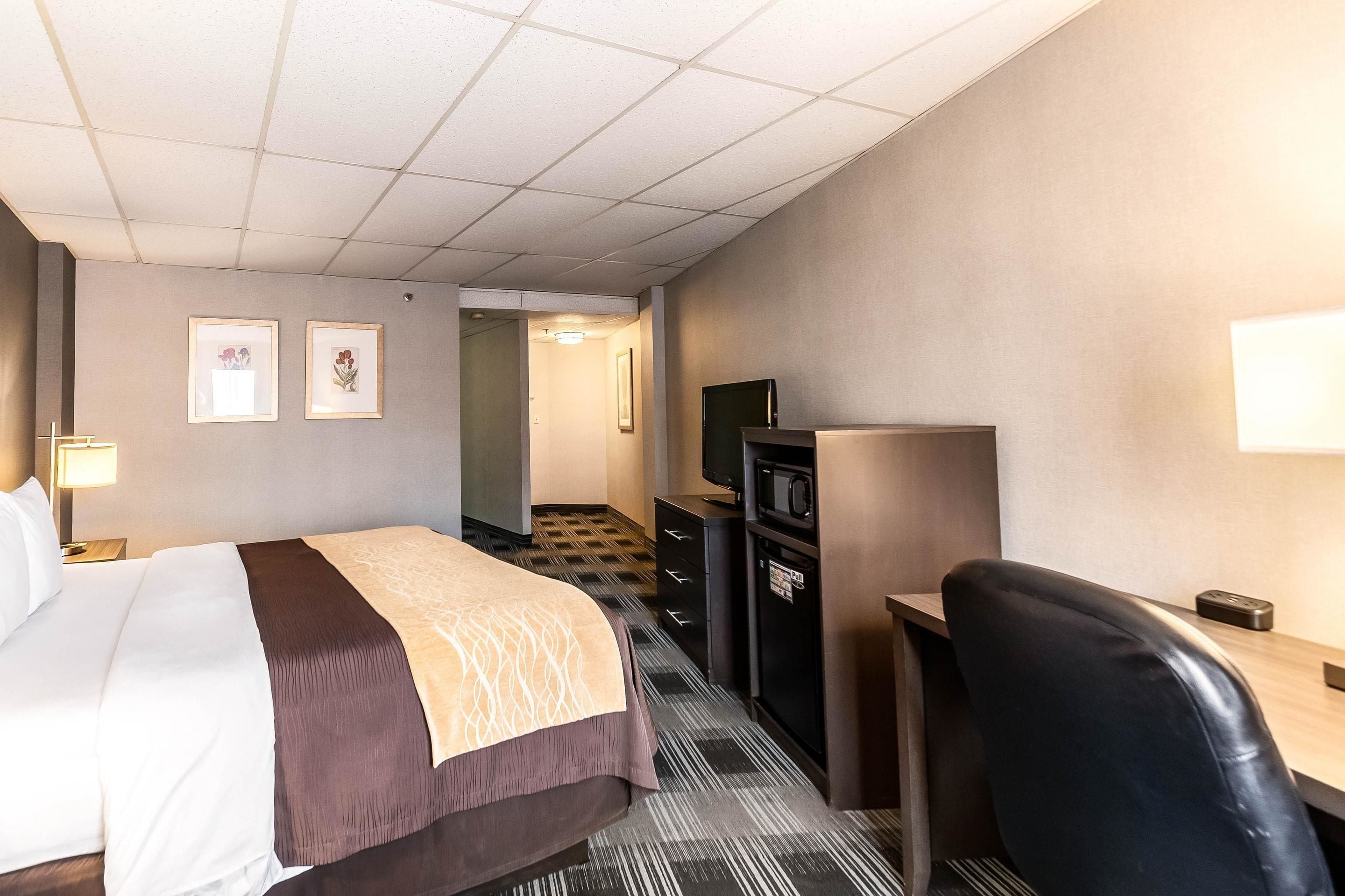 Quarto de hotel com cama, escrivaninha, cadeira, televisão e micro-ondas.