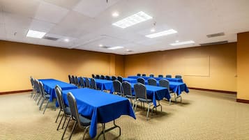 Un salón de conferencias con varias mesas y sillas, suelo alfombrado e iluminación en el techo.