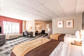 Une chambre d’hôtel avec deux lits, un bureau, une chaise, une télévision et des œuvres d’art encadrées accrochées au mur.