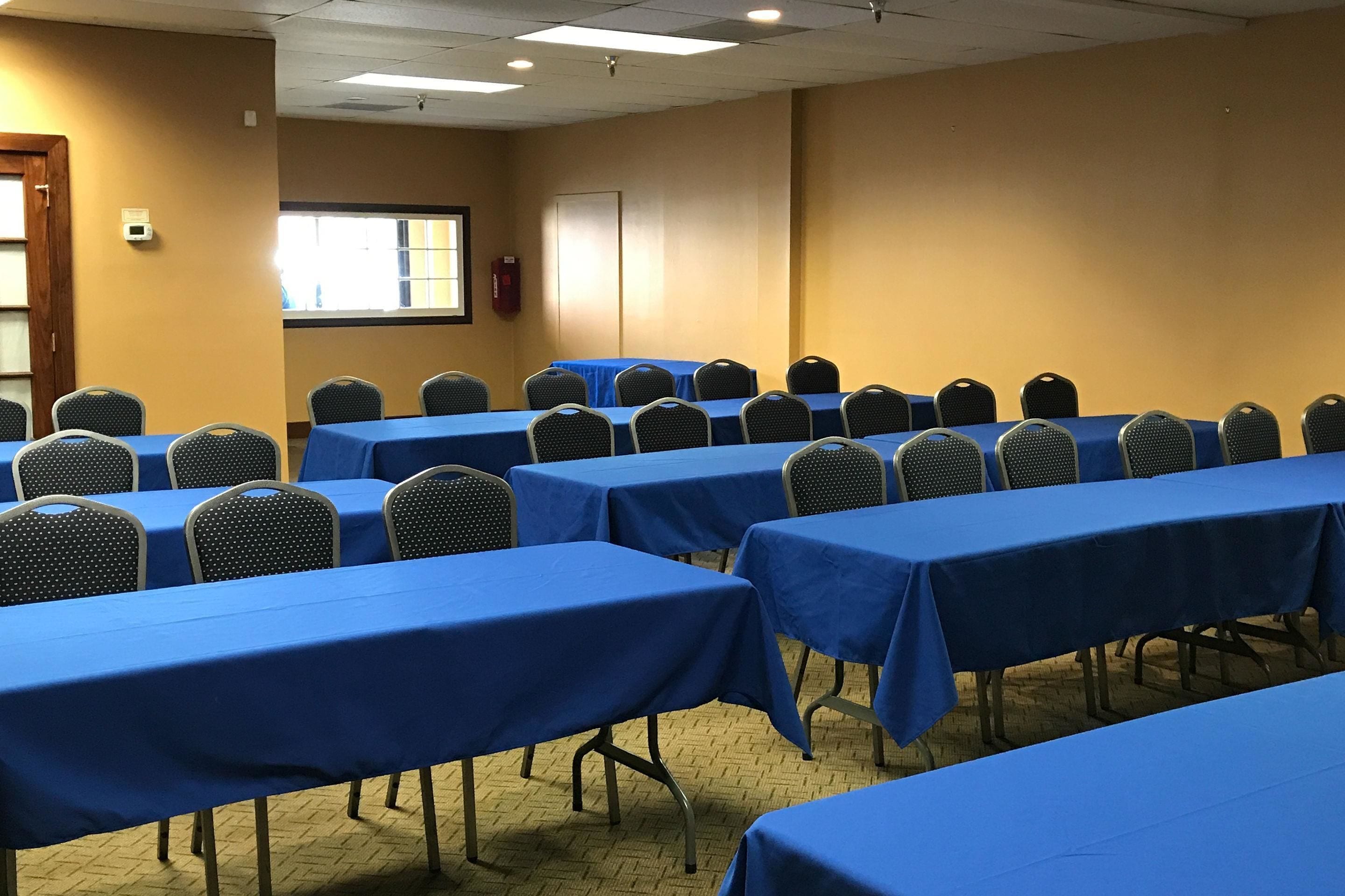 A conference room with multiple tables and chairs, arranged in rows.