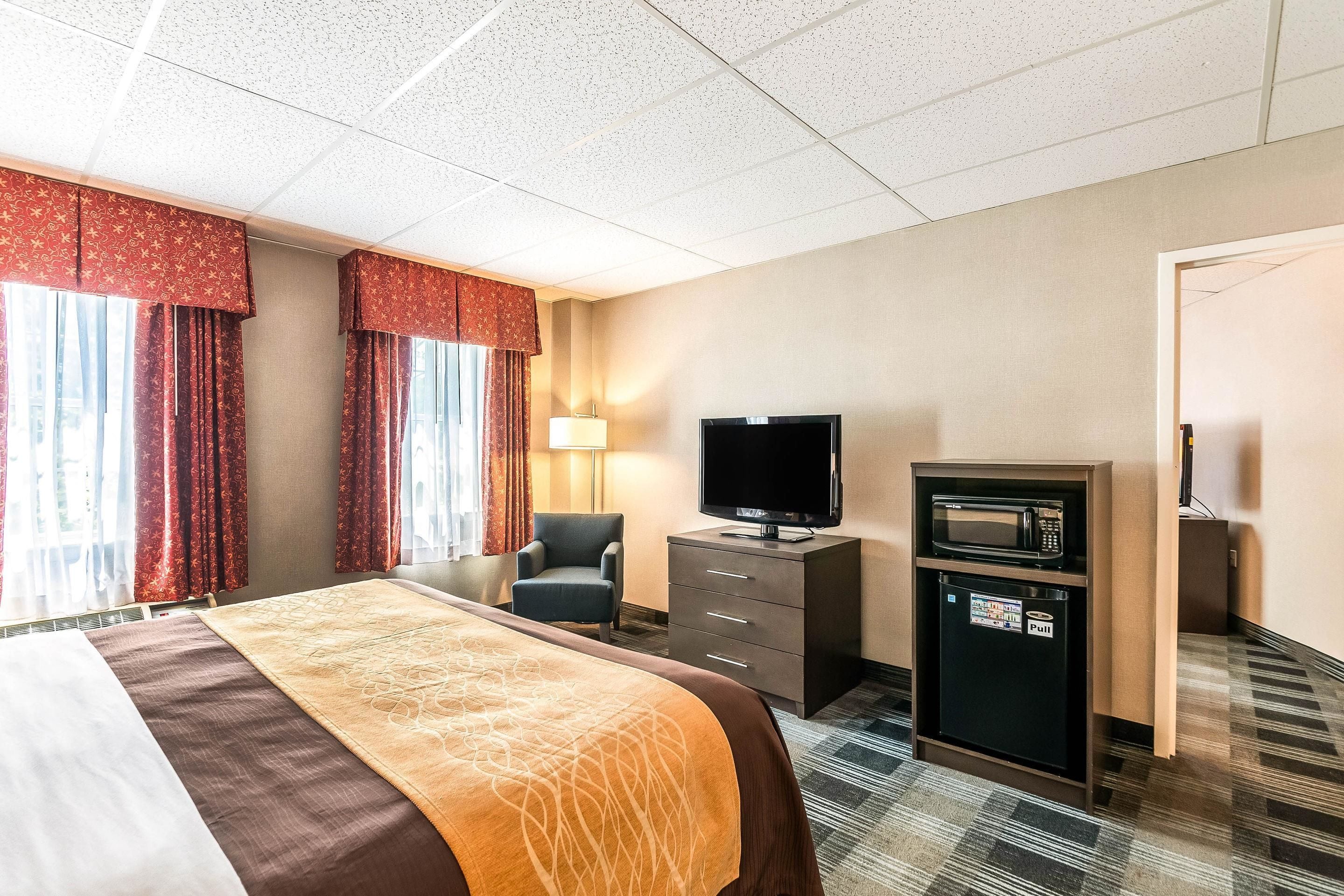 A hotel room with a bed, a television, a small refrigerator, and a desk with a lamp.